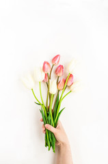 Spring flowers. Feminine hand holding lilac and white tulip flowers bouquet on white background. Flat lay, top view, mock up