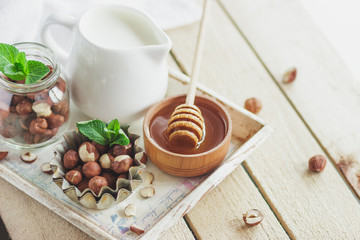 Honey in the wooden bowl, mint leaves, hazelnuts and jar with milk on the wooden tray