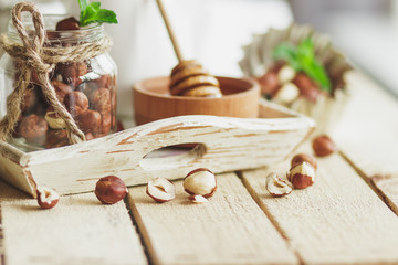Honey in the wooden bowl, mint leaves, hazelnuts and jar with milk on the wooden tray