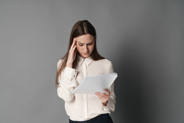 Businesswoman holding his head reading documents. Isolated on gray background. Portrait of...