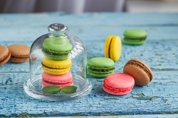 Green, pink and yellow french macarons under the glass on the wooden boards