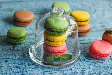 Green, pink and yellow french macarons under the glass on the wooden boards