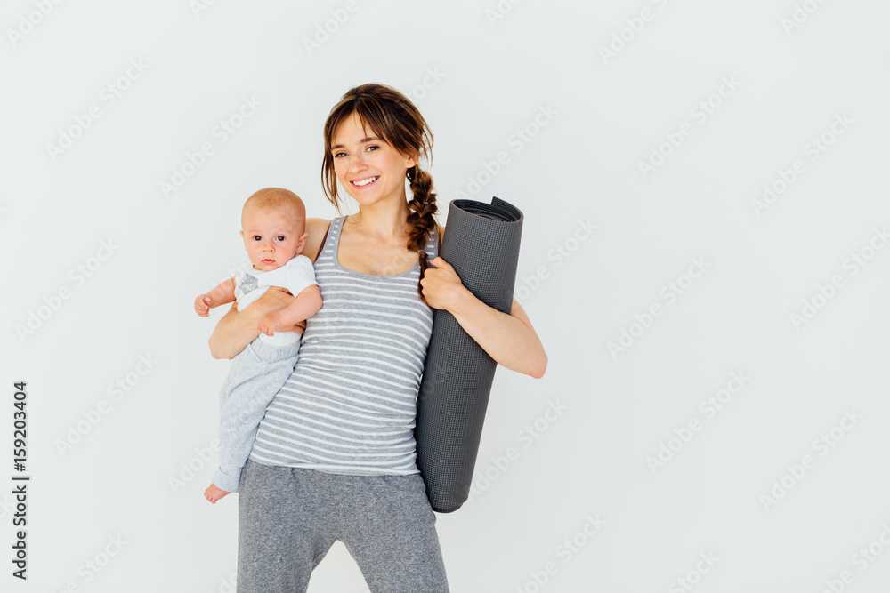 Wall mural sport, motherhood and active lifestyle concept - happy charming sporty mother holding cute little ba