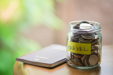 Travel and Saving Concept. Full of coins in clear bottle with yellow label note with Travel word and passport on wooden table.