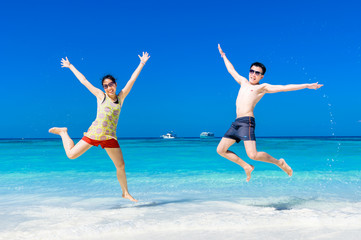 Fototapeta na wymiar The happy Cheerful couple enjoys relaxing and jumping at white sand beach with blue sky and blue sea background.