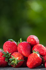 Juicy strawberries in the sun are scattered on a wooden table, against the backdrop of a beautiful...