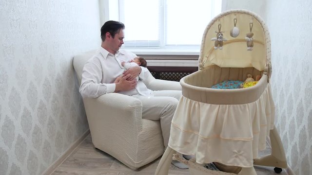dad cradles an infant on background of baby swing with toys