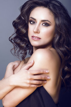 Close up portrait of middle aged beautiful brunette with perfect make-up and naked shoulders looking straight at the camera embracing herself. Studio shot