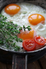 Fried eggs in an old pan with tomatoes, pepper and thyme on a wooden table, Selective focus