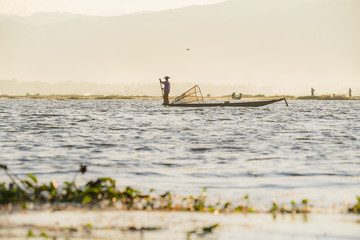 Fototapeta na wymiar Inle Lake, Myanmar - December 7, 2014: Burmese fishermen on boat with fishing net at Inle lake in Myanmar (Burma)