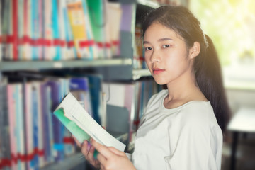 Asian female students holding for selection Book  in library