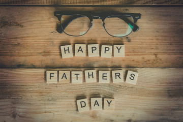 Happy father's day block with glasses on wood background.