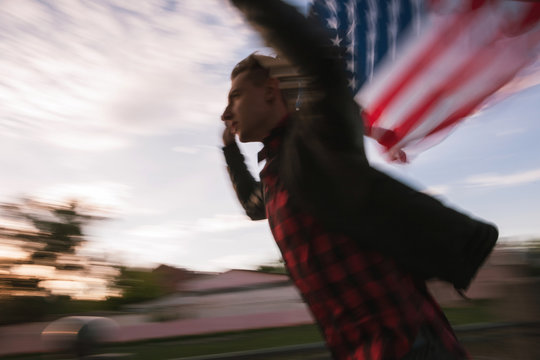 Running blurred guy with US flying flag. Proud american patriot celebrate national event. Teenager on vacation have fun at the independence day