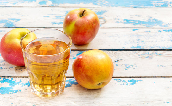 Glass of apple juice and ripe apples on the old wooden table.