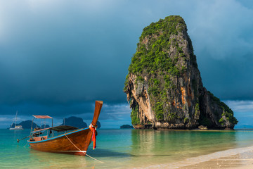 Traditional wooden Thai boat near the shore and high cliff