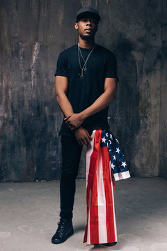 Black man with american flag as accessory on dark background. Casual guy ready to celebrate. Patriot, national event celebration, independence day, pride, immigration, us citizenship concept