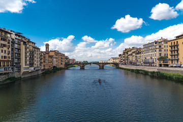 Horizontal composition the River Arno in Florence with puffy clouds and rowers on the water.