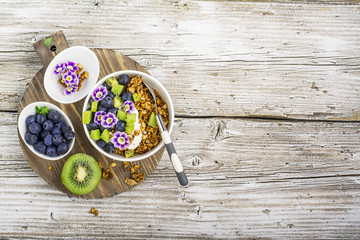 Healthy Breakfast: homemade roasted granola with blueberries, kiwi fruit and edible flowers on wooden background. From the top view. The concept of fitness nutrition
