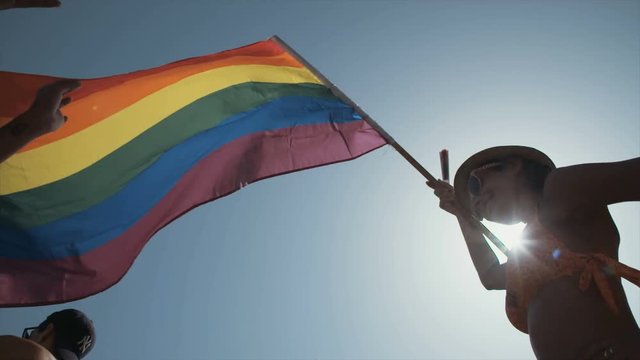 Low angle view of smiling woman waving rainbow flag during pride parade