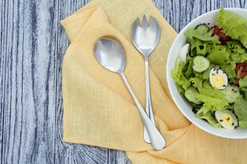 Vegetable salad in white bowl, spoon and fork on grey wooden background
