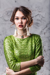 Fototapeta premium portrait of a beautiful young girl with makeup and hairstyle in a bright green dress standing with a smile looking at the dark grey background, close-up