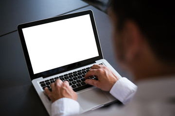 Businessman at a desk in an office typing on a laptop computer with blank white screen