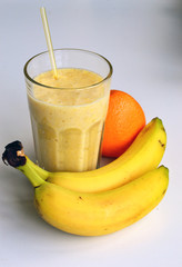 A composition of bananas and orange and a glass with smoothies