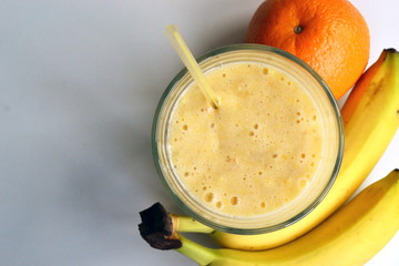 A composition of bananas and orange and a glass with smoothies