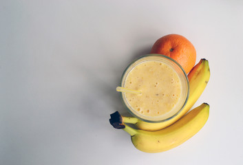 A composition of bananas and orange and a glass with smoothies