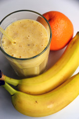 A composition of bananas and orange and a glass with smoothies