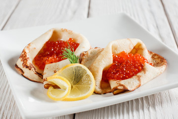 Dessert pancakes with red caviar on white plate. Russian traditional salty crepes with seafood. Shrove tuesday holiday food