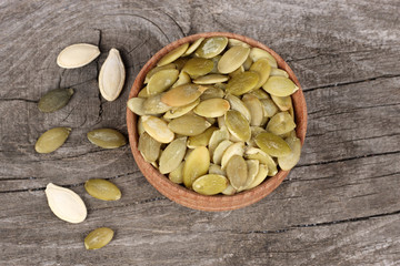 Pumpkin seeds in wooden bowl on wooden background top view with copy space