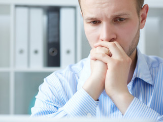 Businessman being depressed by working in office. Frustrated young handsome man looking exhausted while sitting at his working place and wrking on computer.