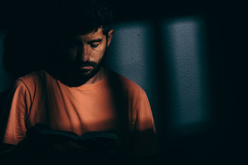 Prisoner man in dark cell reading a book or bible