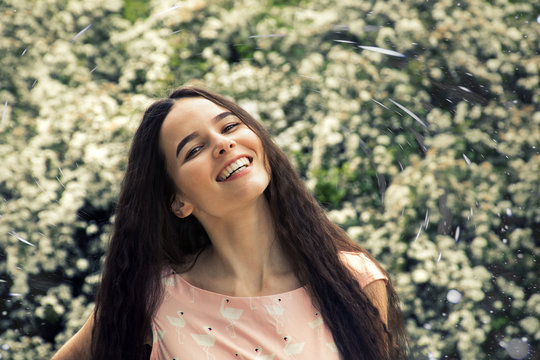 The girl smiles with joy against a white wall of flowers