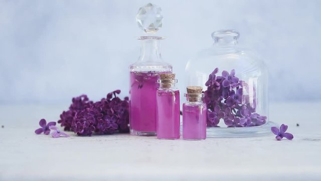 Someone hand placing corc in lilac essence in glass vial, with fresh lilac flowers
