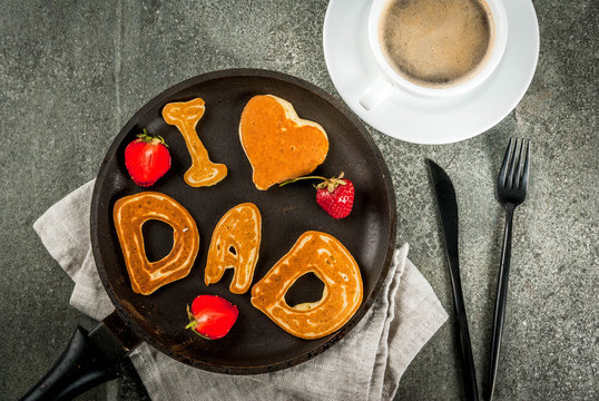 Celebrating Father's Day. Breakfast. The idea for a hearty and delicious breakfast: pancakes in form of congratulations - I love dad. In a frying pan, coffee mug and strawberries. Top view copy space