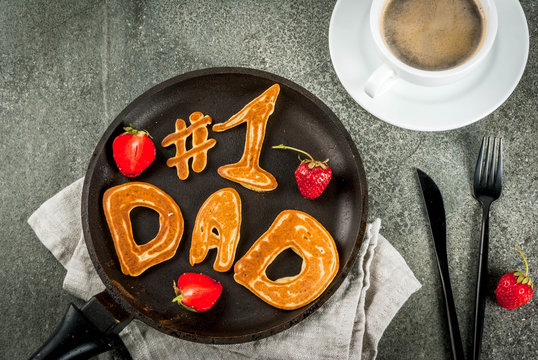Celebrating Father's Day. Breakfast. The idea for a hearty and delicious breakfast: pancakes in form of congratulations - #1 dad. In a frying pan, coffee mug and strawberries. Top view copy space