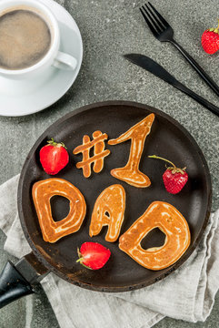 Celebrating Father's Day. Breakfast. The idea for a hearty and delicious breakfast: pancakes in form of congratulations - #1 dad. In a frying pan, coffee mug and strawberries. Top view copy space