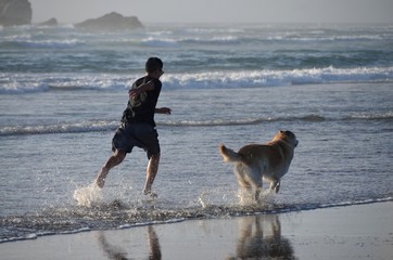 Teenage Boy Running In The Surf With His Dog