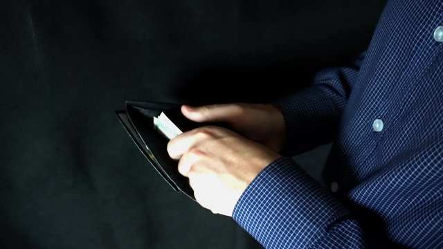 puts money in wallet. A man opens a leather purse and puts bills.