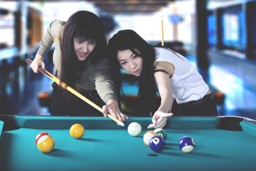 Two beautiful women playing billiard