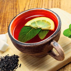 Delicious healthy hot herbal drink made of Ceylon black tea, fresh mint leaves and lemon in a rustic clay mug on a wooden table.