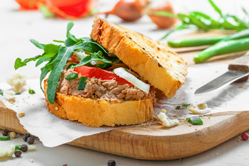 Delicious sandwich made of toasts, tuna, tomato, onion and arugula with ingredients on a white table. Traditional healthy food.