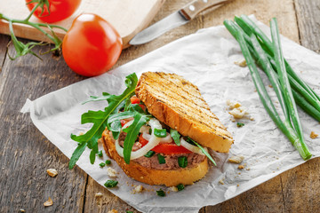 Classic tuna salad sandwich with tomato, onion and arugula on a table. Delicious healthy meal made of fish, vegetables and toasts.