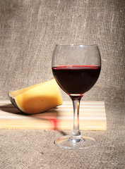 Glass with red wine grapes and chees on wooden table.