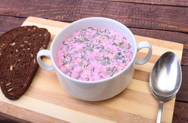 Popular spring cold soup okroshka with yoghurt. Okroshka in a bowl and slices bread on wooden table. Selective focus