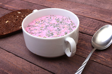 Popular spring cold soup okroshka with yoghurt. Okroshka in a bowl and slices bread on wooden table. Selective focus