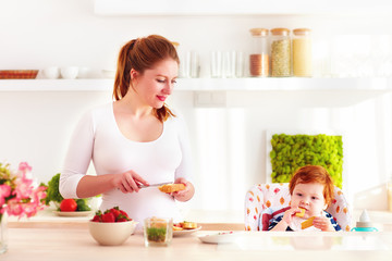 young mother and infant baby in high chair having breakfast in the kitchen