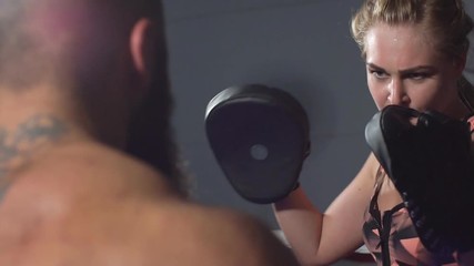 Male boxing trainer exercising with female. Coach is sparring with a young athlete. Slow motion